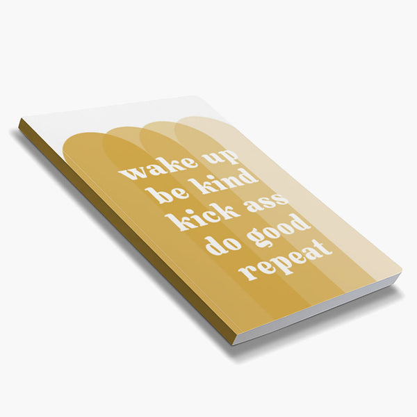 Front cover of dot grid 72-page notebook with soft touch cover; "wake up be kind kick ass do good repeat" in white text atop overlapping arches in shades of gold