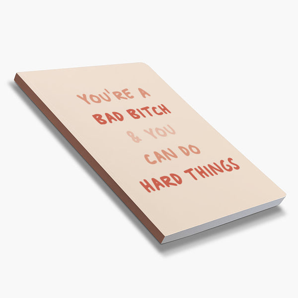 Front cover of dot grid 72-page notebook with soft touch cover "You're a bad bitch & you can do hard things" in shades of pink with blush background