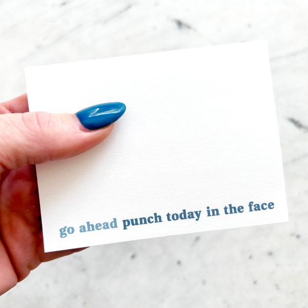 hand holding 4"W x 3"L sticky notepad; "go ahead ~ punch today in the face" in blue lowercase font along bottom on white background