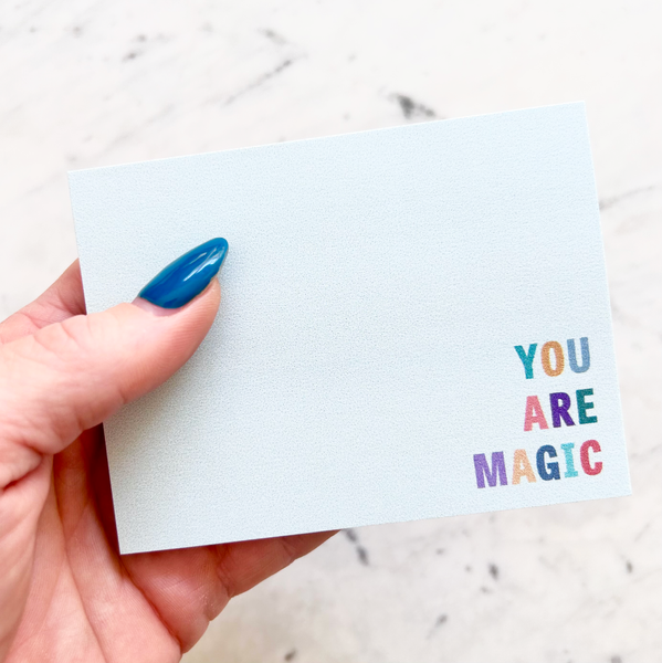 hand holding 4"W x 3"L sticky notepad; "you are magic" in colorful block letters in lower right corner on light teal background