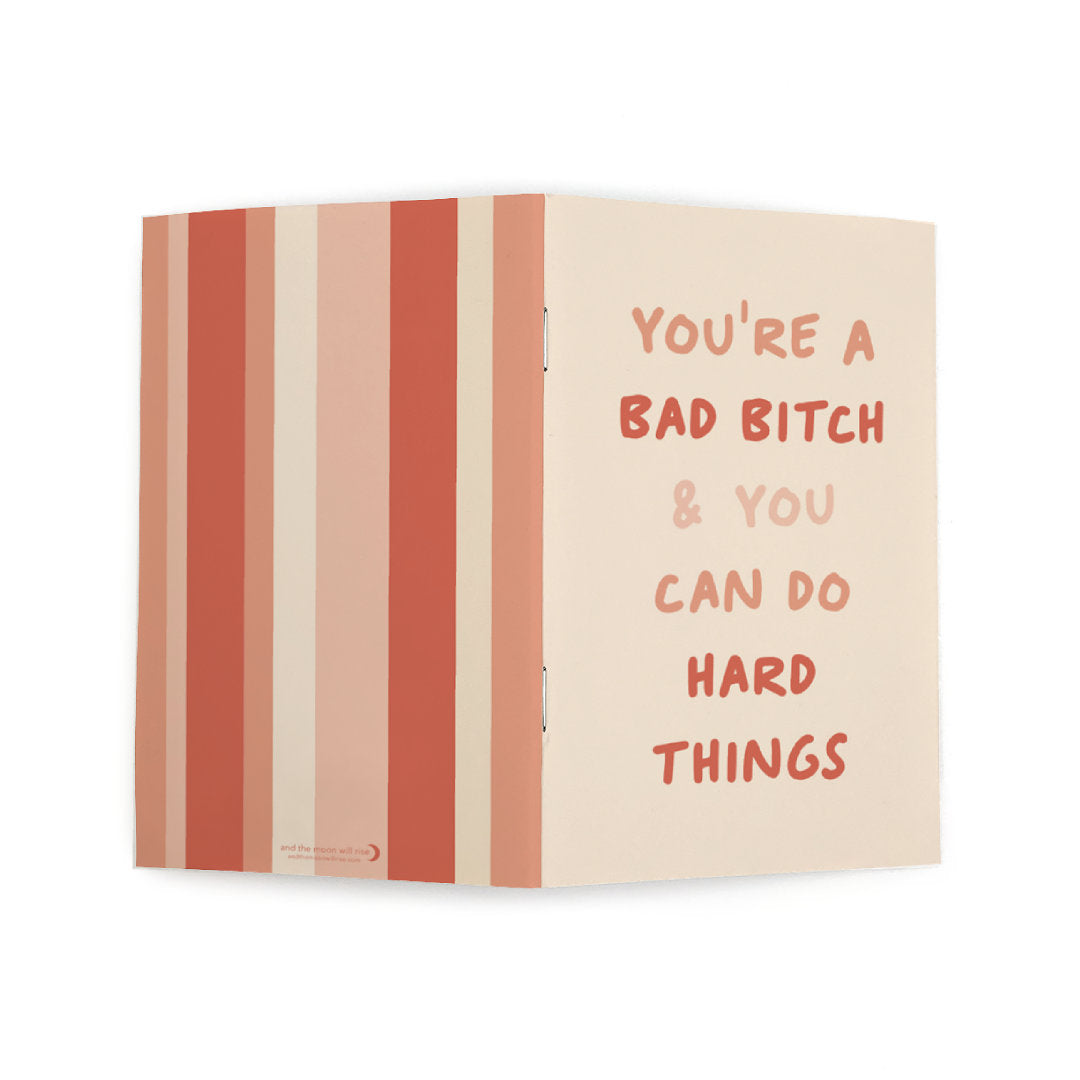 Pocket notebook with front cover reading YOU'RE A BAD BITCH & YOU CAN DO HARD THINGS on blush and back cover with various widths of pink and coral strips
