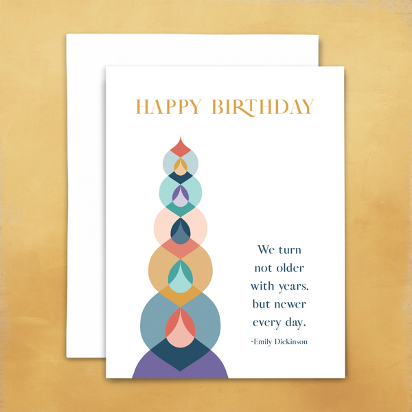 Happy birthday greeting card with blank interior; text reads "happy birthday" with quote from Emily Dickinson "we turn not older with years, but newer every day"; white card with colorful geometric shapes; with white envelope; shown on goldenrod background