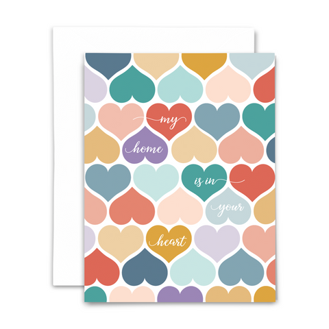 "My home is in your heart" greeting card; white script font on top of patterned hearts in various colors- blues, teals, golds, pinks, purples; white interior with white envelope