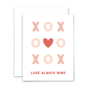 "Love always wins" greeting card; tic tac toe game of pink Xs and Os with red heart in the center on white background; blank interior with white envelope 