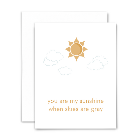 "You are my sunshine when skies are gray" blank greeting card. Golden-colored font and sun with light gray clouds on white background; with white envelope