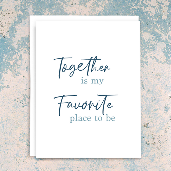 "Together is my favorite place to be" greeting card; dark blue script and light blue serif fonts on white background; blank interior with white envelope. Shown photographed on distressed blue and cream plaster background.