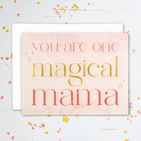 Blank greeting card "you are one magical mama"; pink and gold font on light pink marbled background with gold stars; with white envelope; shown on white wood background with pink and gold confetti