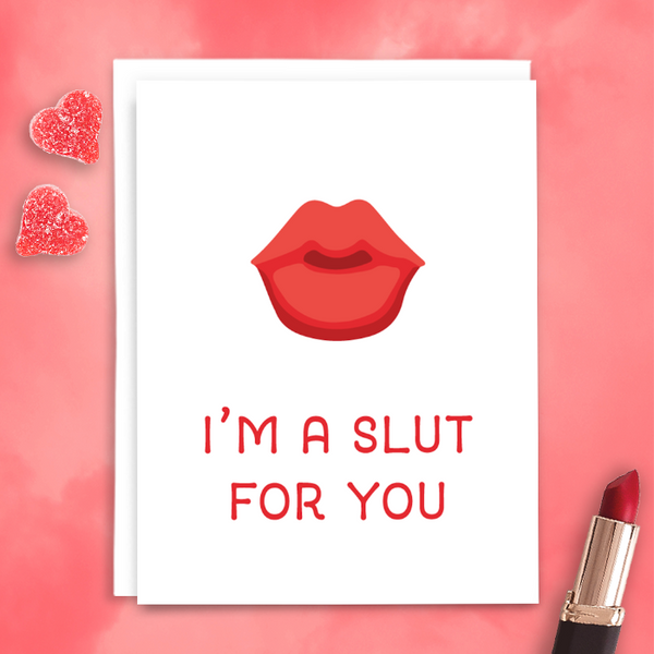 "I'm a slut for you" in red lettering with red and pink cartoon lips on white background; blank interior with white envelope. Photographed on pink background with red lipstick and red candy hearts